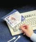 Preview: Auf dem Bild sieht man eine Hand, die einen leicht transparenten Beutel mit "PC Buds" hält. Daneben liegt eine weiße Tastatur und zwei Wattestäbchen auf einem blauen Untergrund.
