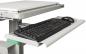 Preview: The image shows a desk with a pull-out keyboard tray. On the tray, there is a black, flat keyboard and next to it a black computer mouse. The surface is light gray.