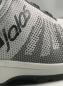 Preview: Das Bild zeigt einen sportlichen Schuh in Grau und Weiß mit einem modernen, strukturierten Obermaterial. Der Markenname ist seitlich in Schwarz aufgedruckt. Die Sohle ist dunkel und rutschfest.