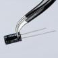 Preview: The image shows a pair of tweezers holding a cylindrical, black capacitor. The capacitor has two metal terminals and markings in white and gold.