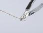 Preview: The image shows a pair of pliers gripping a thin copper wire. The pliers have black handles and a shiny top. The background is light and neutral.