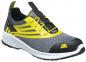 Preview: The shoe is a gray sneaker with yellow accents. It has a sporty design, a textured surface, and a black, reinforced toe cap. The laces are in the center.