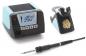 Preview: The image displays a soldering system with a heating station in light blue and black. It features a digital display and buttons. Next to the station, there is a soldering iron with a cable and a holder.