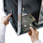 Preview: A person is holding a computer circuit board in their hand and is inserting it into a metallic case. In the background, cooling fins are visible. The focus is on the circuit board.