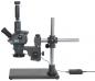 Preview: The image shows a microscope with a stable, black base. It has a telescope-like lens, a lateral eyepiece, and a vertical mount that supports the work area. A cable terminates in a control unit.
