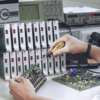 Preview: A hand holds a screwdriver and works on a circuit board. In the background are several devices with red displays, representing test and measurement instruments.