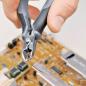 Preview: Eine Hand hält eine Zange, die dünnen Kupferdraht schneidet. Im Hintergrund ist eine Leiterplatte mit verschiedenen elektronischen Bauteilen und einer goldenen Oberfläche zu sehen.