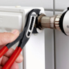 Preview: A hand is holding pliers on a heating pipe. The pipe is made of metal and mounted on a white radiator. The pliers have black and red handles.