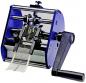 Preview: The image shows a mechanical device with a hand crank. Two rollers grasp a long, narrow strip that slides through the device. The colors are predominantly blue and black.