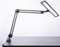 Preview: The image shows a black desk lamp with a flexible arm system. The lamp head is elongated and has a bright light source that is angled downwards.