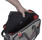Preview: A hand places a black laptop into a gray bag with red lining. The bag has two handles and an open zipper.