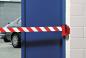 Preview: The image shows a blue door secured with a red-and-white barrier. In the background, a gray car is parked in front of the door. The adjacent wall is white.