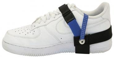 Das Bild zeigt einen weißen Sneaker mit flacher Sohle. An der Außenseite des Schuhs ist ein schwarzes und blaues Halteband befestigt, das zur Stabilisierung dient.