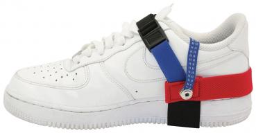 Das Bild zeigt einen weißen Sneaker mit verschiedenen farbigen Riemen: rot, blau und schwarz, die seitlich am Schuh befestigt sind. Der Schuh hat eine klassische Sneakerform mit Schnürsenkeln.