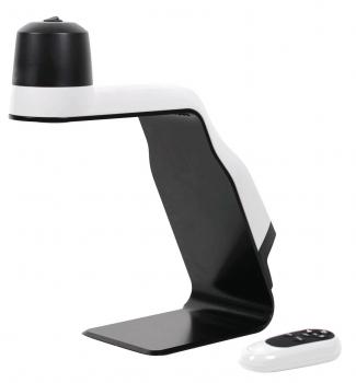 Das Bild zeigt eine moderne Tischlampe in Schwarz und Weiß. Sie hat eine kreative, geschwungene Form und eine runde Lampenoberseite. Neben der Lampe liegt eine kleine Fernbedienung.