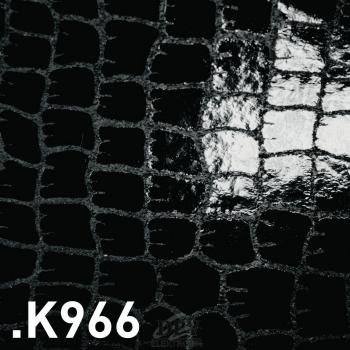 The image displays a black, shiny surface with a pattern of rectangular scales reminiscent of crocodile leather. The texture is irregular and slightly raised.