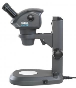 The image shows a dark-colored microscope with a thick, round head and a magnifying glass. It stands on a sturdy base with an illuminated area and a switch.