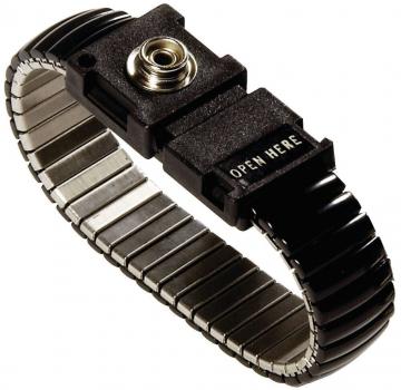 Das Bild zeigt ein schwarzes, metallisches Armband mit einer flexiblen, federnden Struktur. In der Mitte befindet sich ein rechteckiger Verschluss mit der Aufschrift "OPEN HERE".