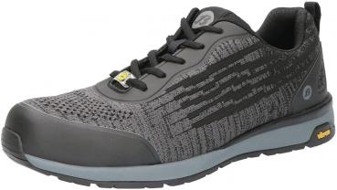 Der Schuh ist sportlich und modern, hauptsächlich in Schwarz mit grauen und metallischen Akzenten. Er hat eine strukturiert wirkende Oberfläche, Schnürsenkel und eine robuste, gummierte Sohle.