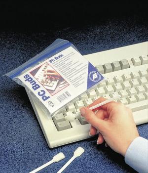 Auf dem Bild sieht man eine Hand, die einen leicht transparenten Beutel mit "PC Buds" hält. Daneben liegt eine weiße Tastatur und zwei Wattestäbchen auf einem blauen Untergrund.