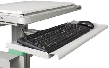 The image shows a desk with a pull-out keyboard tray. On the tray, there is a black, flat keyboard and next to it a black computer mouse. The surface is light gray.