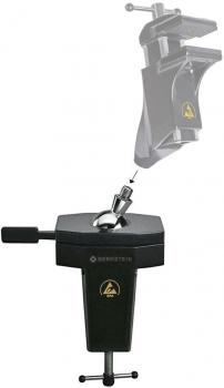 The image shows a black holding device with an adjustable clamp on top. It is square, has a handle, and a screw for attachment. A movable arm is visible on top.