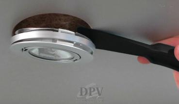 The image shows a handle lifting a round, silver ceiling lamp. The lamp has a transparent area in the middle and is encased in a dark, circular frame.