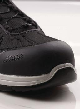 The image shows the front part of a black shoe with a sturdy rubber sole and a reinforced toe. The shoe has a textile upper and laces.