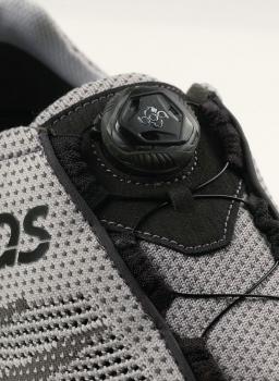 Das Bild zeigt einen grauen Sportschuh. Oben befindet sich ein schwarzes Schnürsystem mit einem runden Klickmechanismus. Der Schuh hat ein atmungsaktives Mesh-Material.