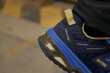 Das Bild zeigt einen nahen Ausschnitt eines Sportschuhs in Blau und Schwarz. Der Schuh hat gelbe Akzente und eine profilierte Sohle, die für guten Halt sorgt.