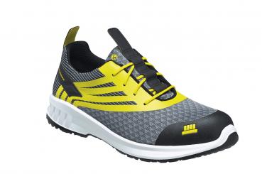 Der Schuh ist ein grauer Sneaker mit gelben Akzenten. Er hat ein sportliches Design, eine strukturierte Oberfläche und eine schwarze, verstärkte Zehenkappe. Die Schnürsenkel sind in der Mitte.
