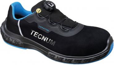 Der Schuh ist schwarz mit blauen Akzenten. Er hat eine Sohle mit Profil und eine Schnürung mit einem besonderen Verschlusssystem. Auf der Seite steht "TECNUM".