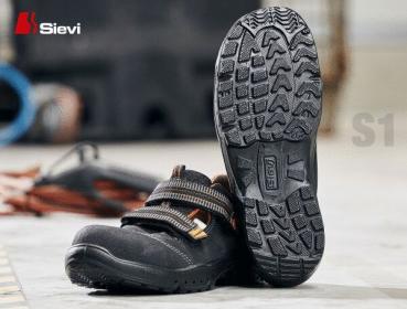 The image shows a pair of black safety shoes with a non-slip sole. The shoes have wide straps over the foot and are suitable for use in an industrial environment.