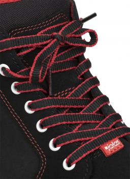 Das Bild zeigt einen schwarzen Schuh mit roten Schnürsenkeln. Die Schnürsenkel sind aufwendig gebunden und verlaufen durch weiße Ösen. Ein kleiner roter Aufnäher ist sichtbar.