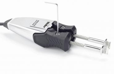 The image shows a hair clipper with a metallic casing and a black rubber grip. On the front, there are two blades that can be pulled apart. A small tool stands upright.