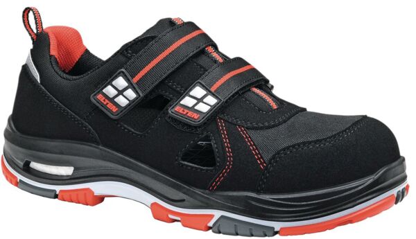 The shoe is black with red accents. It has two Velcro straps, a sporty shape, and a padded sole. The material appears sturdy and is suitable for work use.