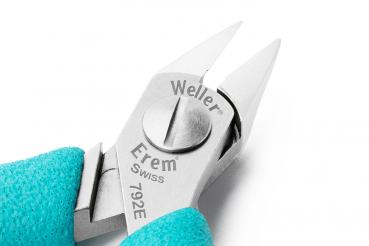 Das Bild zeigt eine präzise Zange mit zwei spitzen Klingen und einem zentralen Drehknopf. Der Griff ist türkisfarben, und die Klingen sind aus glänzendem Metall.