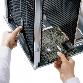 A person is holding a computer circuit board in their hand and is inserting it into a metallic case. In the background, cooling fins are visible. The focus is on the circuit board.