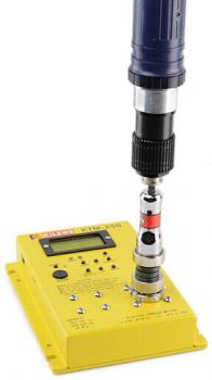 The image displays a yellow, rectangular device with buttons and a screen. Above it, there is a drill-like tool attached that has an attachment.
