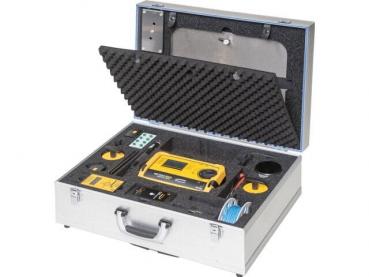 The image displays an open, silver suitcase. Inside, there is a yellow device, numerous buttons, cables, and compartments, all neatly organized in a foam-padded interior.