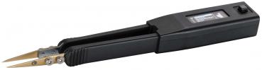 The image displays a black device with two golden clamps, which is open, and a rectangular casing. Next to the device, there is a black cap or protective cover.