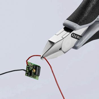 A pair of pliers holds two wires, a red one and a black one, which are attached to a small green circuit. The background is bright and neutral.