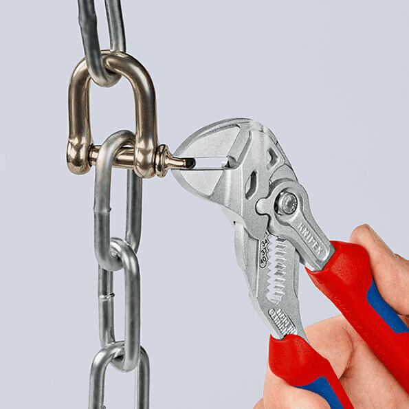 The image shows a pair of pliers gripping a metal eyelet. The pliers have red and blue handles and are aimed at a chain made of shiny metal.