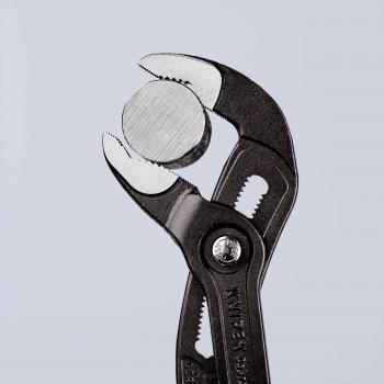 The image shows a pair of pliers with a round metal disc in between. The pliers are black with a textured surface and have a distinctive mechanism for adjusting the opening.