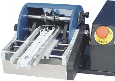 Das Bild zeigt eine Maschine zum Fräsen oder Schneiden. Sie hat zwei große Rollen, die gedreht werden, und eine lange Rutsche für das Material. Auf der rechten Seite befindet sich ein Not-Aus-Knopf.