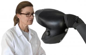 Das Bild zeigt eine Frau in einem weißen Laborkittel mit Brille, die konzentriert auf ein futuristisch aussehendes Gerät schaut. Das Gerät hat eine geschwungene Form und eine Linse.