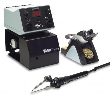 The image shows a soldering station with a digital temperature controller on top, a black base, and a soldering iron on the left side. On the right, there is a holder with cleaning wool.