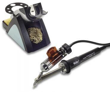 The image shows a soldering iron set: A soldering iron with a black handle and metal tip, connected by a cable. Next to it is a stand with a sponge and a small metal brush for cleaning.