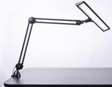 The image shows a black desk lamp with a flexible arm system. The lamp head is elongated and has a bright light source that is angled downwards.