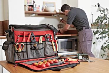 The bag is rectangular with a gray and black design. It features a wide carrying handle, several zippers, and a red diagonal stripe. A side pocket is also present.